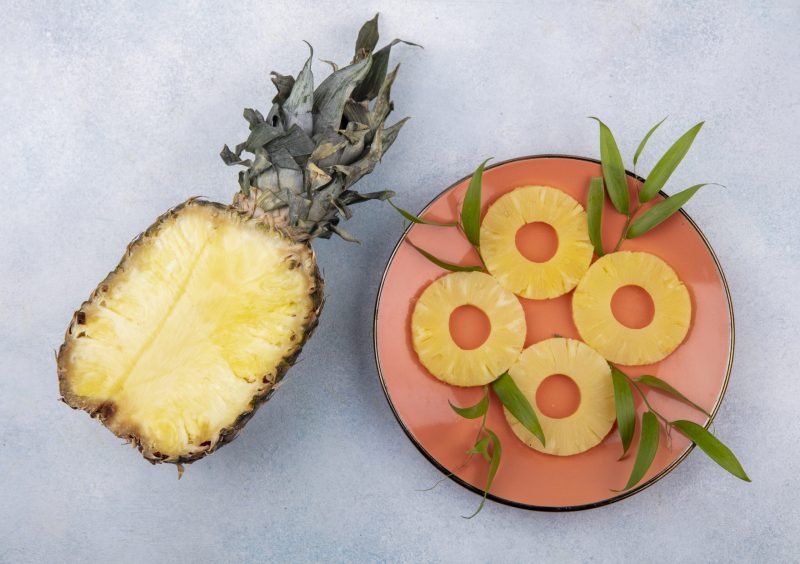 top view of half of pineapple with pineapple slices in plate on white background